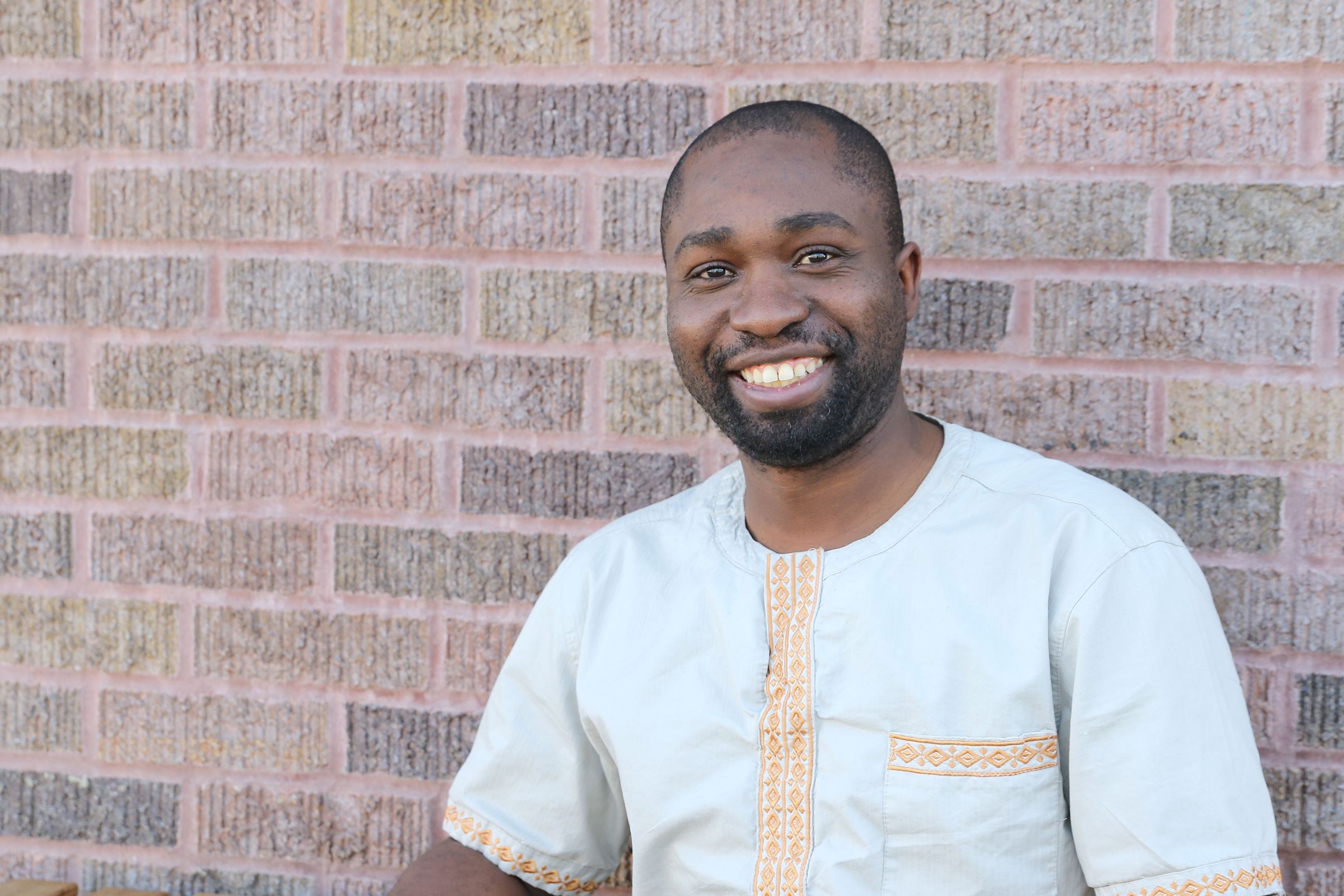 Henry smiling and sitting outside Amore Coffee against a brick wall